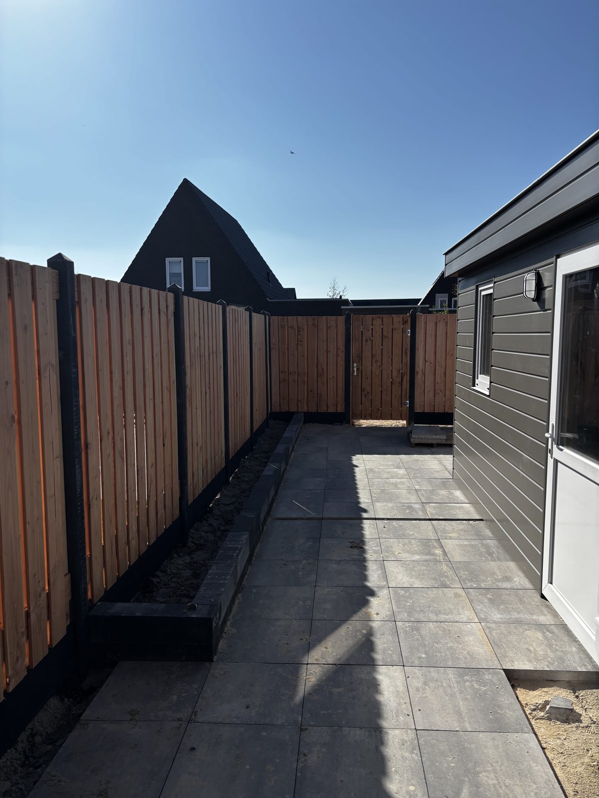 Douglas schutting met zwarte palen en tuinpoort langs een nieuw terras