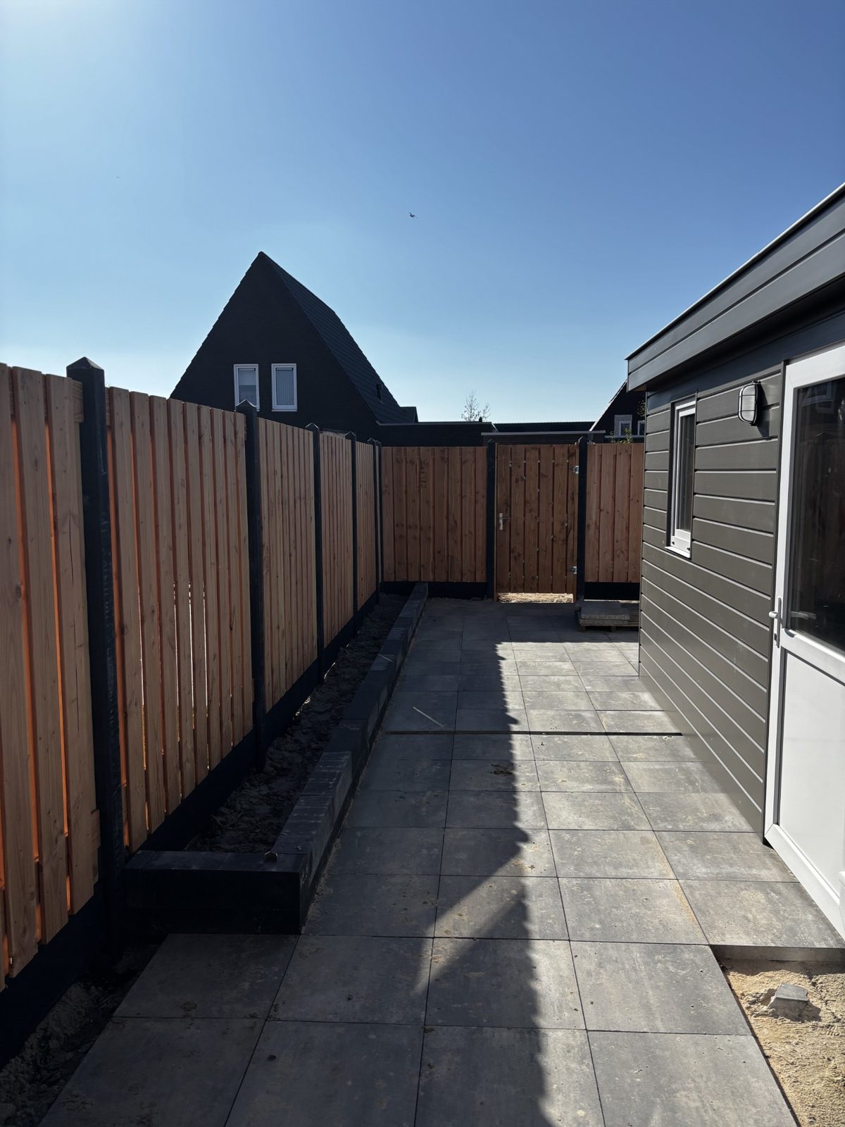 Lange douglas schutting met zwarte palen langs een tuinpad